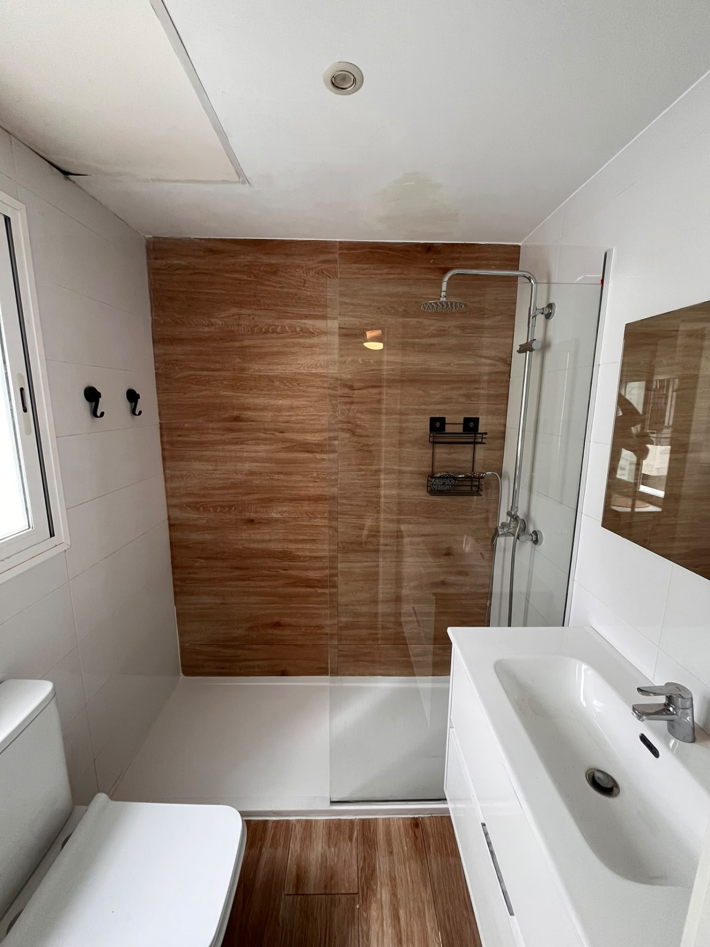 Baño con ducha, alicatado efecto madera y mueble de lavabo blanco