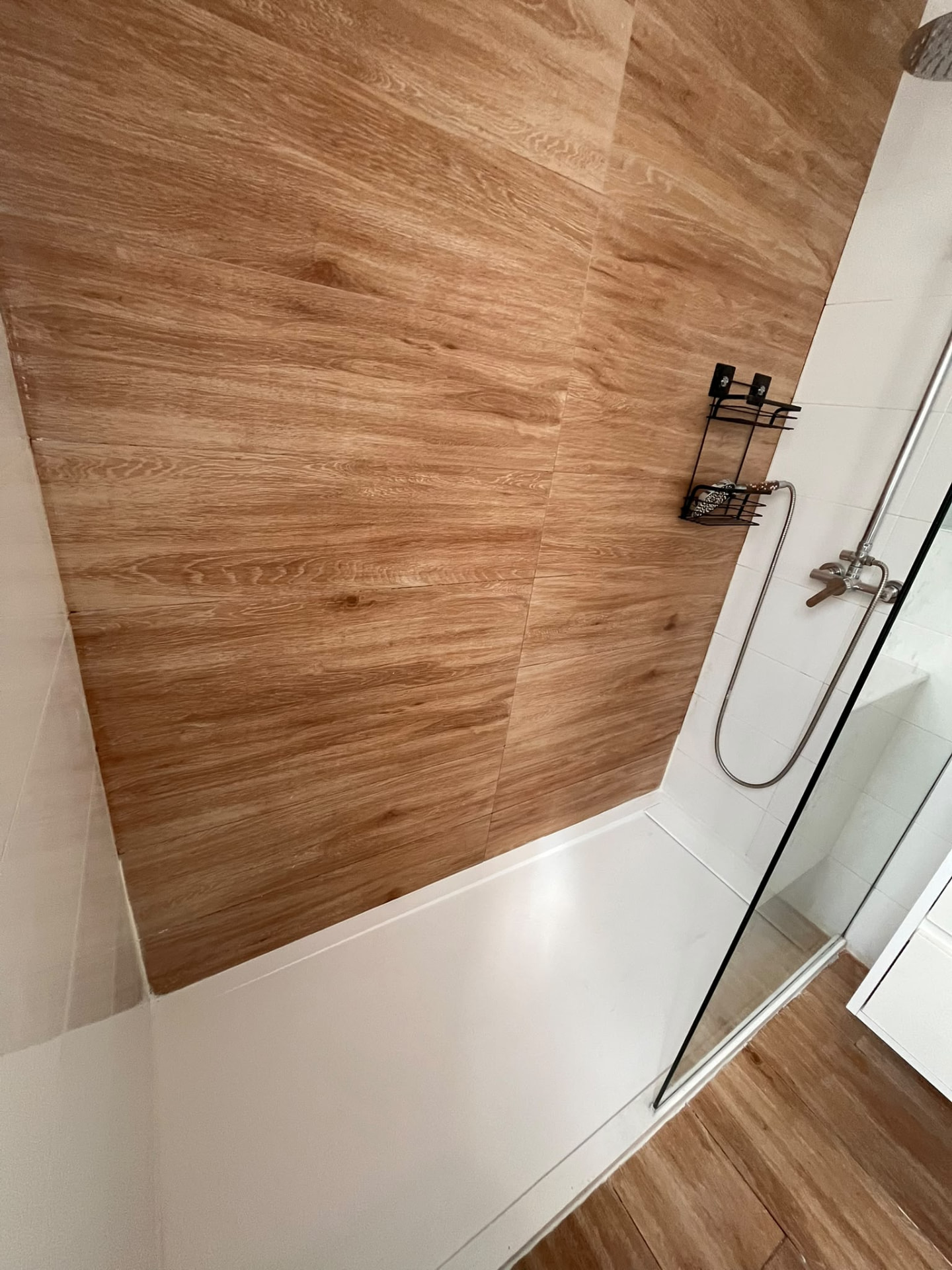 Detalle de ducha con plato blanco y alicatado efecto madera