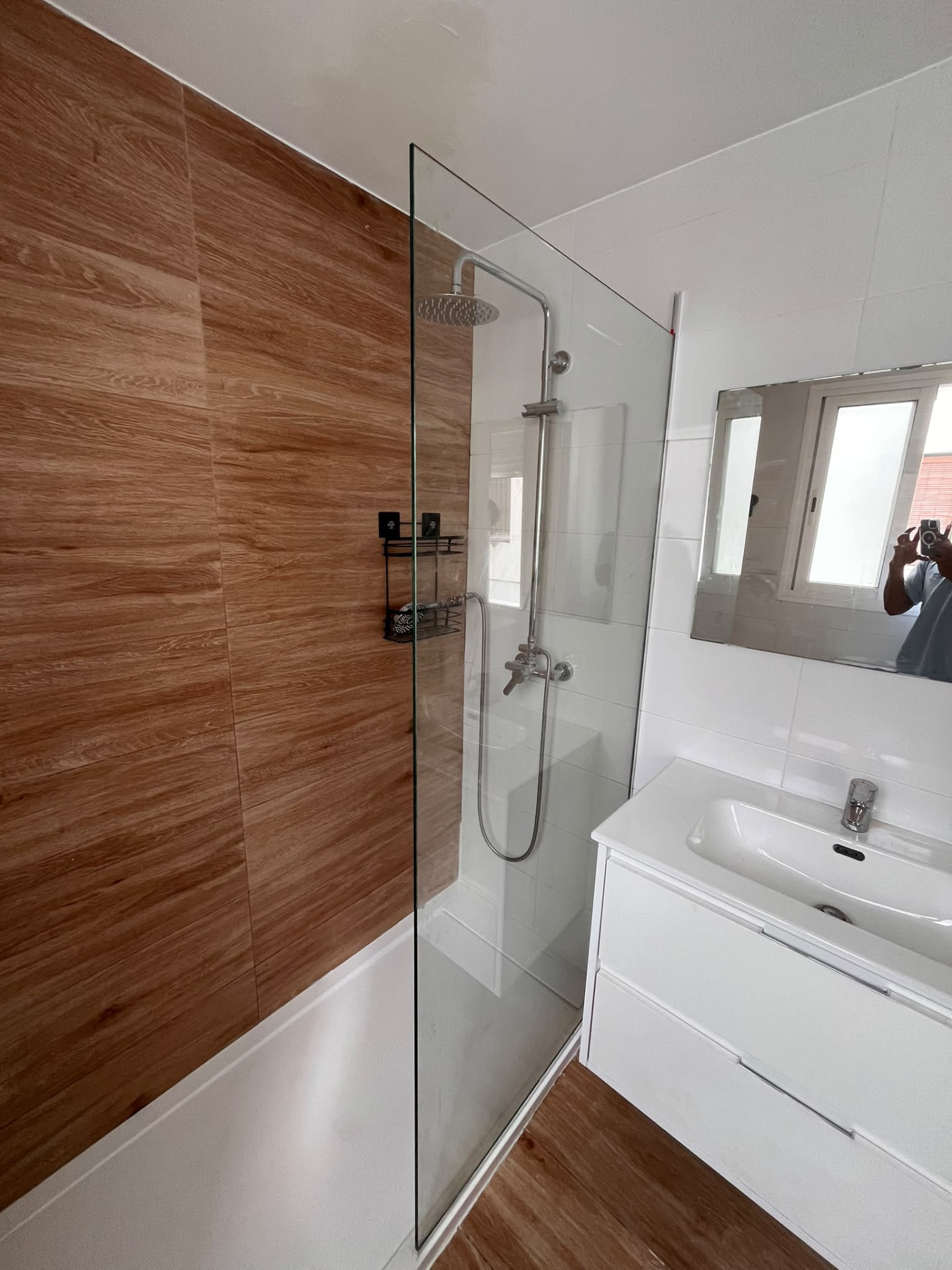 Ducha con mampara de cristal junto a mueble de lavabo blanco